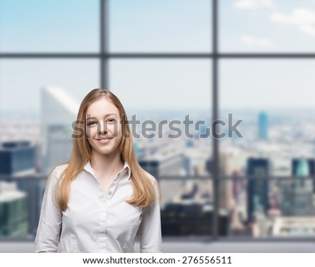 Young beautiful business lady is smiling in the panoramic glass office. New York background. A concept of internship.
