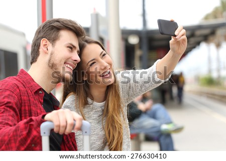 Couple of travelers photographing a selfie with a smartphone in a train station