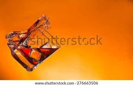 Whiskey ice drink with splash on orange background