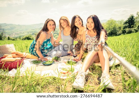 Multi-ethnic group of women enjoying picnic in the countryside and taking a picture with selfie stick - Four girls on vacation having fun