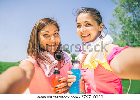 Two young athletic women taking a picture after running in a park - Best friends training together outdoors,Both girls have towels, drinks and phone arm holder