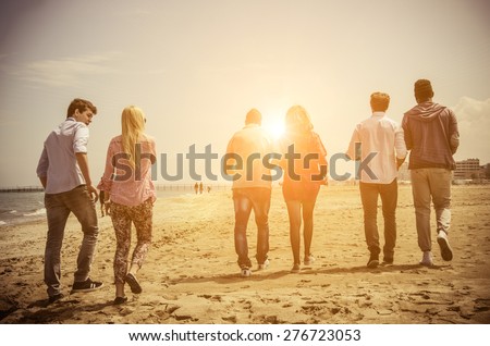 Multi-ethnic group of friends walking on the beach and talking - Group of young adults silhouettes at sunset