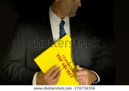 Top Secret Classified business, legal and government concept showing a man in a black suit pulling a Top Secret folder dossier out of his jacket. Dramatic lighting highlights the Top Secret folder Royalty-Free Stock Photo #276736106