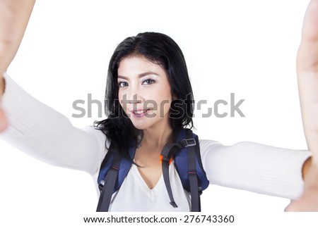 Portrait of young woman carrying backpack for hiking and taking selfie picture in the studio