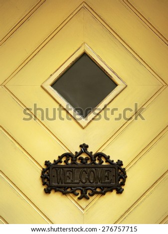 The yellow door with diamond form window and Welcome inscription on it