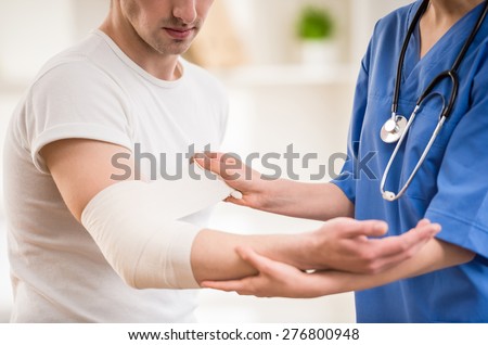 Close-up of female doctor with stethoscope  bandaging hand of male patient. Royalty-Free Stock Photo #276800948