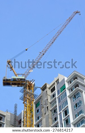 Big crane and incomplete skyscraper with blue sky as background with copy space. Building and construction concept photography.