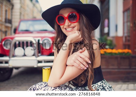 Beautiful fashionable woman in a hat and sunglasses posing over red car