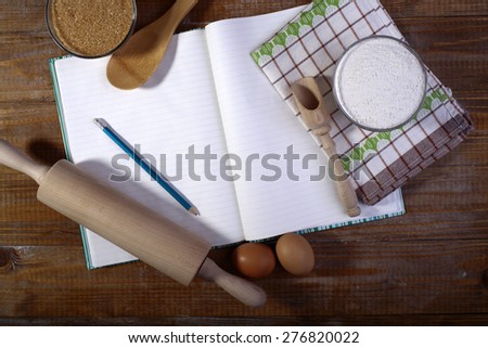 Set of ingredients and appliances for cooking with opened recipe book and towel on wooden table top, horizontal picture