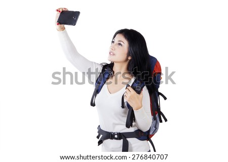 Female hiker using smartphone to take selfie picture while carrying backpack, isolated on white background