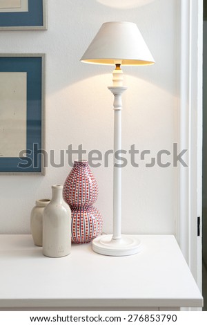Close up still life detail view of two decorative porcelain pieces sitting together on a fireplace mantelpiece next to a lit lamp, house interior design. Aspirational lifestyle, indoors.