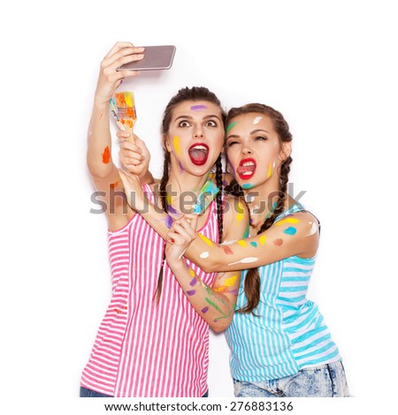 Paint on the face of pretty girl friends having fun. Women with paintbrush  Taking Self Portrait with Their Phone. White background not isolated