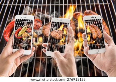 friends using smartphones to take photos of sausage and pork chop and vegetables on the flaming grill.