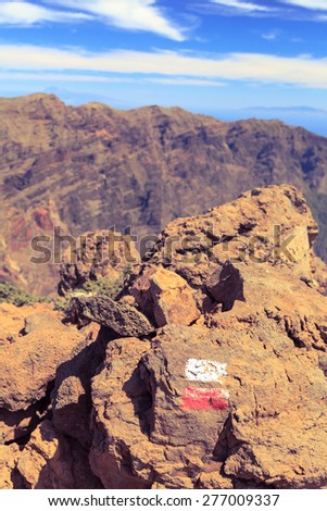 Beautiful mountains landscape with trail sign white and red on rock. Canary Islands on ocean in the background. Hiking or trekking path.
