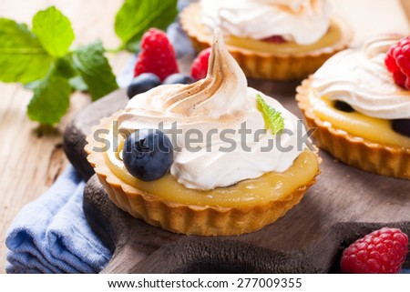 Delicious homemade tartlets served with lemon, lime curd cream, berries and meringue on old cutting board.  Selective focus.