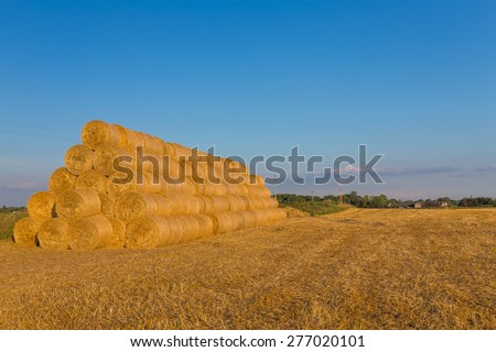 Piled hay bales on a field against blue sky at sunset time