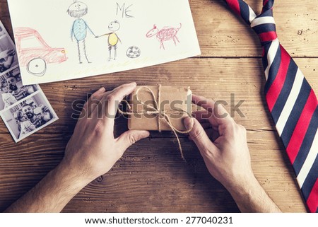 pictures of father and daughter, childs drawing, present and tie laid on wooden desk backround.