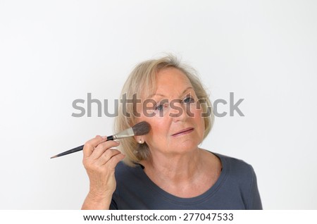 Attractive middle-aged woman applying makeup to her forehead with a large soft cosmetics brush to smooth out the signs of wrinkles and aging
