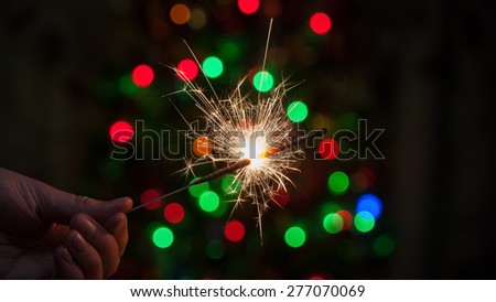 Bengal fire burns in his hand against the background of the Christmas tree.