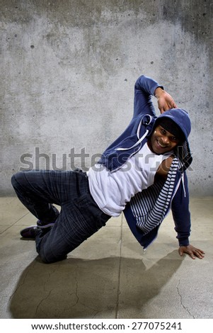 Active young black male dancing hip hop style in an urban setting.  He is wearing a blue hoodie and is on a concrete background with copyspace.