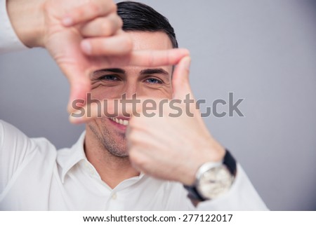 Businessman making frame with fingers over gray background and looking at camera