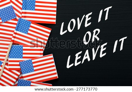 Miniature flags of the United States of America on a blackboard next to the phrase Love It Or Leave It in white text