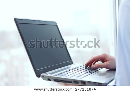 Using technologies. Picture of man holding computer in front of window.