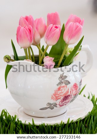 Tulips in teapot on green grass.