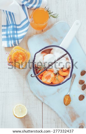 Homemade apricot marmalade. High angle view of sugared apricots in a pan, preserving jar and apricot juice, rustic style,  on a wooden surface. Natural light 