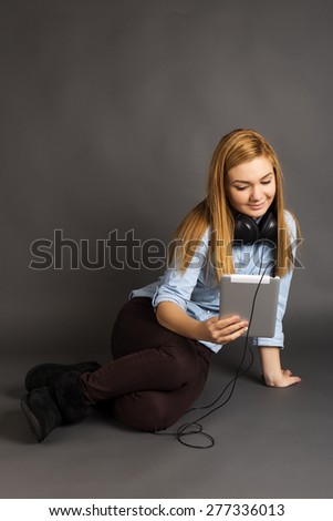 Beautiful teenage girl sitting on the floor with headphone and her tablet over gray