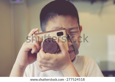 Asian boy holding a wooden camera toy.