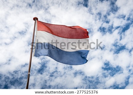 Flag of the Kingdom of the Netherlands in red, white and blue strips of fabric fastened at a flagpole or a ship and blowing in the wind.