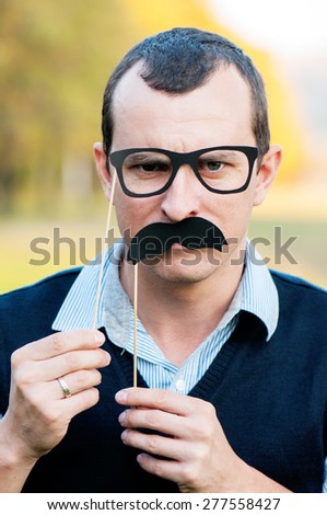 strict man with decorative glasses and moustaches on a stick looks in the camera