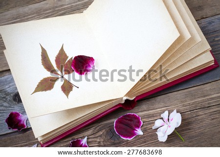 open book with herbarium leaves and petals of geraniums on the page. Still on the old wooden textured boards