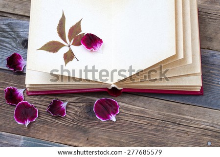 open book with herbarium leaves and petals of geraniums on the page. Still on the old wooden textured boards