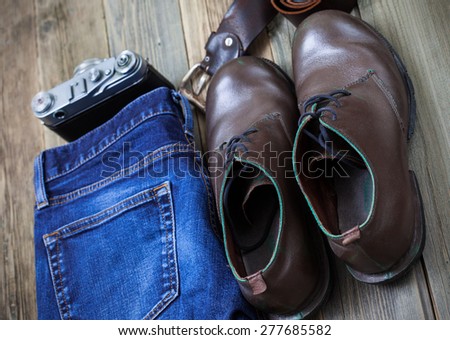 Still life with blue jeans, brown boots, leather belt and rangefinder camera on aged textured boards