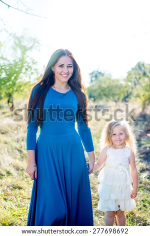 Picture of beautiful young lady in a blue dress with little girl walking at park or forest