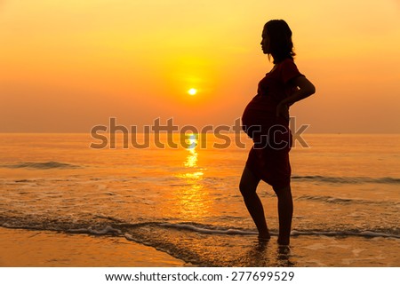 Silhouette pregnant woman sunrise beach.