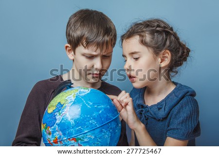 Teenage boy with a girl looking at a globe girl opened her mouth on a gray  background