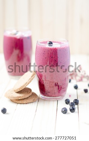 Cranberry and black currant smoothie in glass with cookies on a white wooden background
