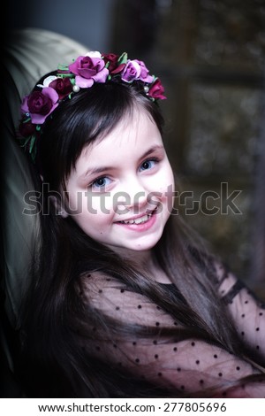 Portrai of cute small blue-eyed brunette smiling girl with wreath of purple roses looking forward, vertical picture