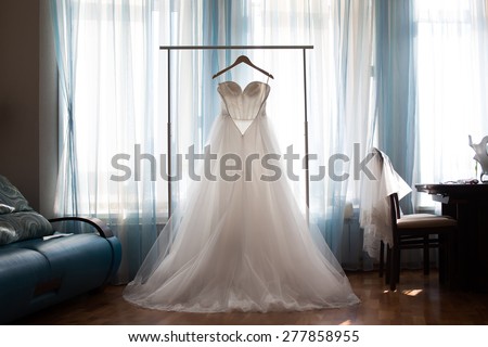 The perfect wedding dress with a full skirt on a hanger in the room of the bride with blue curtains Royalty-Free Stock Photo #277858955