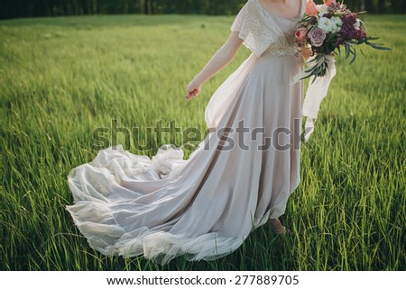 a bride in a beautiful dress with a train holding a bouquet of flowers and greenery
