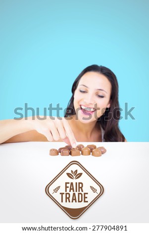 Pretty brunette picking out chocolate against blue background with vignette