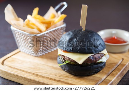 cheeseburger on black buns with fresh cucumber and tomato on wooden board with fries. close up photo