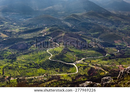 Country road through vegetation with sun rays lighting parts of the natural landscape in greece
