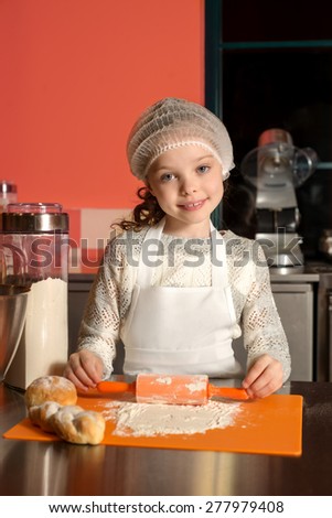 Little child girl sitting at table and playing with dough and flour, bakery, cooking