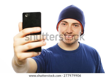 Life style, tehnology and people concept: a young man in shirt holding mobile phone and making photo of himself while standing against white background.