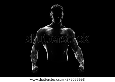 Silhouette of a strong bodybuilder. Confident young fitness man with strong hands and clenched fists. Black and white photo. Dramatic light. Royalty-Free Stock Photo #278055668