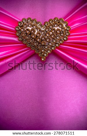 Gold heart on a background of pink cloth.